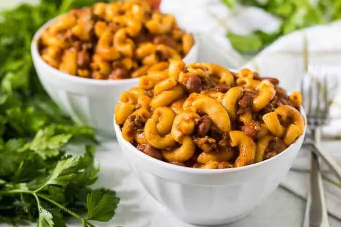 Two bowls of the instant pot chili mac surrounded by parsley.