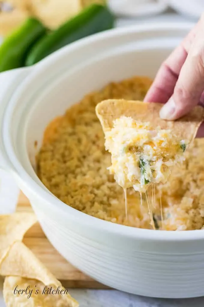 A tortilla chip being dipped into the jalapeno popper dip.