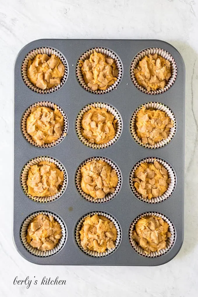 Twelve muffin liners have been half filled with raw batter.