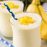 Two finished banana pineapple smoothies garnished with diced fresh pineapple.