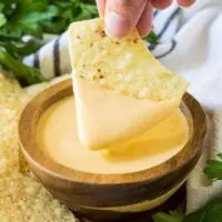 A tortilla chip being dipped into the finished cheese dip.