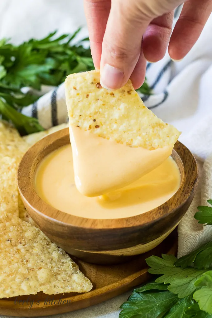 A tortilla chip being dipped into the finished cheese dip.