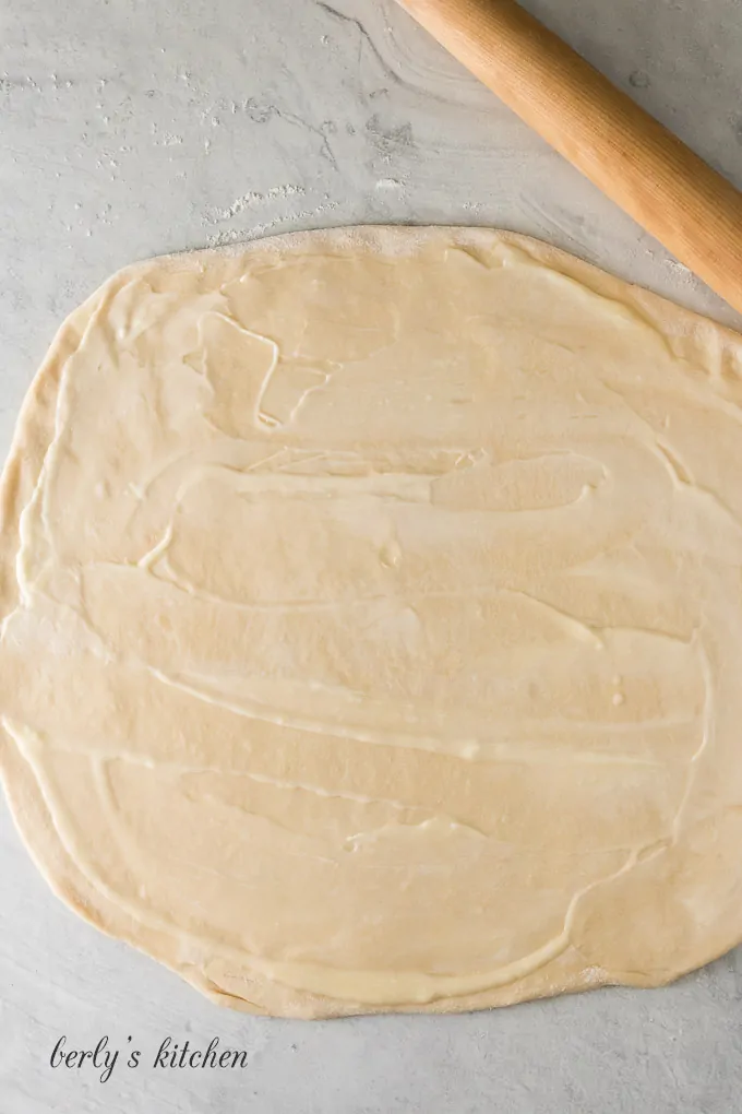 The cinnamon roll dough has been buttered and rolled out.