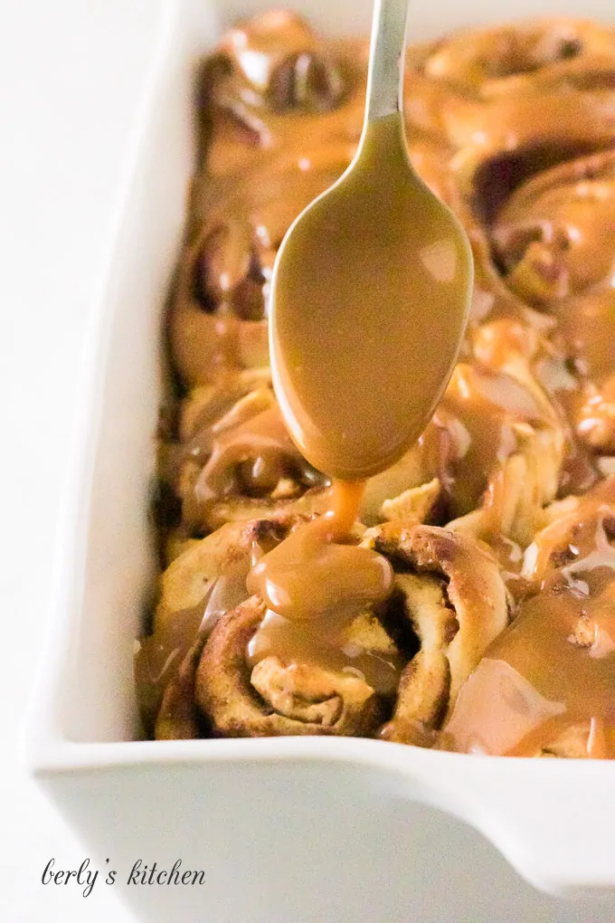 Warm caramel sauce being drizzled over the finished cinnamon rolls.