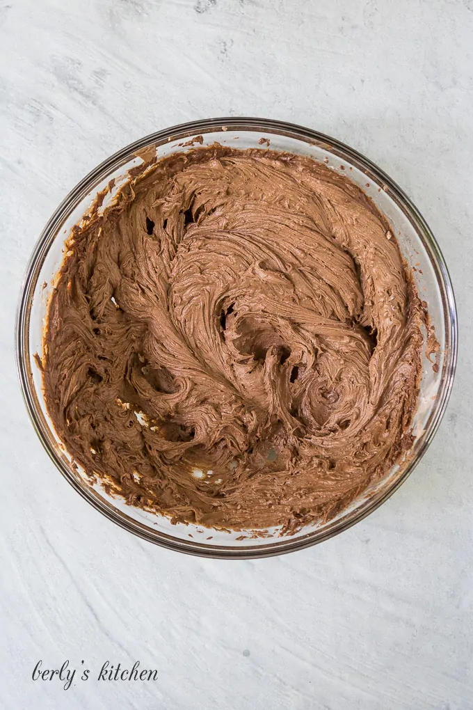 The chocolate buttercream frosting has been mixed in a glass mixing bowl.