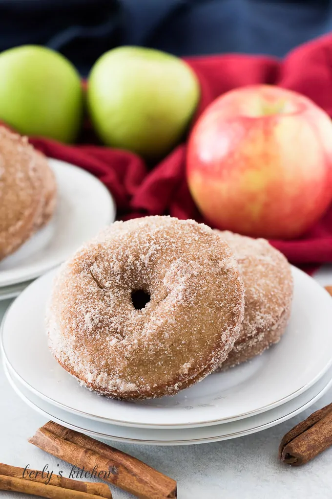 Two finished apple donuts sitting on a small white plate.