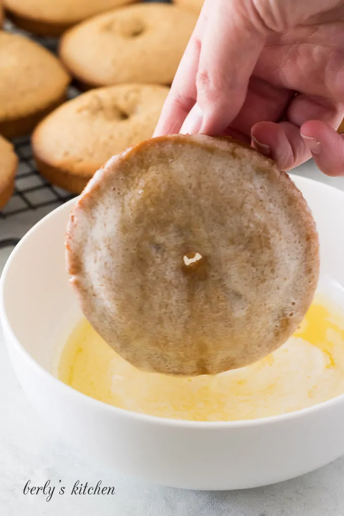 A baked apple cider donut being dipped into melted butter.