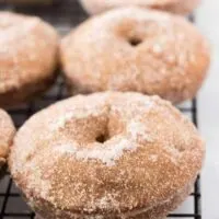 Six finished apple cider donuts sitting on a cooling rack.