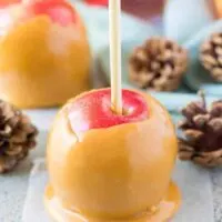 A caramel apple on wax paper surrounded by fall decorations.