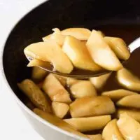 A large metal spoon scooping out the finished cinnamon apples.