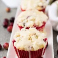 Three cranberry orange muffins drizzled with glaze on a plate.