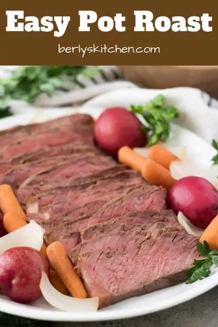 Sliced beef pot roast surrounded by carrots, onions, and potatoes.