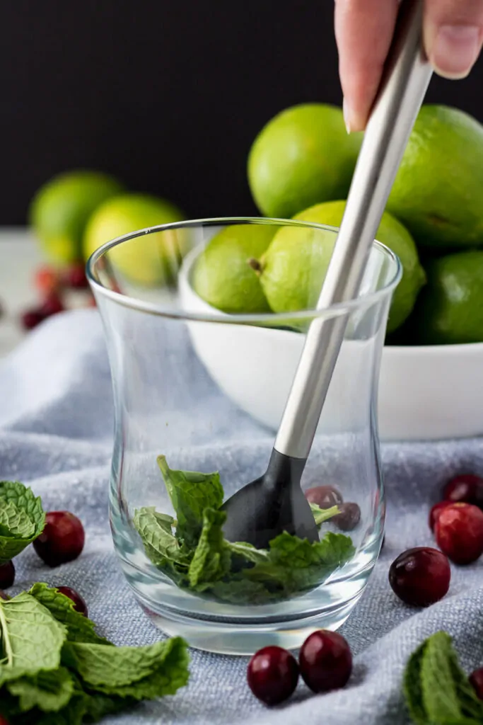 A muddler being used to grind together fresh mint and sugar.