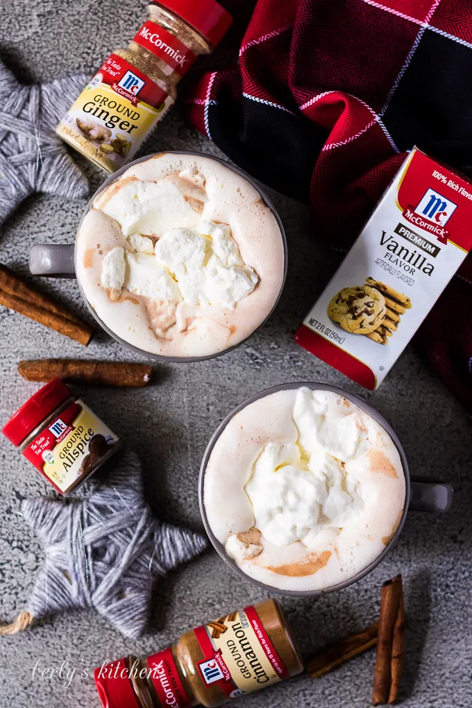 An aerial view of two mugs of cocoa topped with whipped cream.