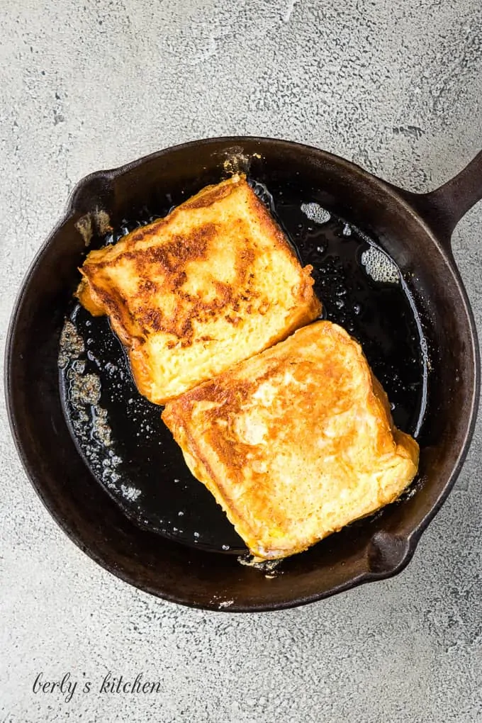 Two pieces of toast being cooked in an iron skillet.