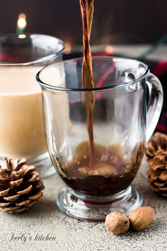 The coffee being poured into a large clear glass mug.