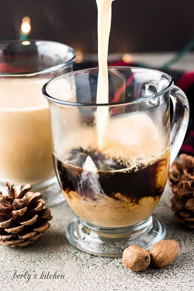 Eggnog being poured into the clear mug with brewed coffee.