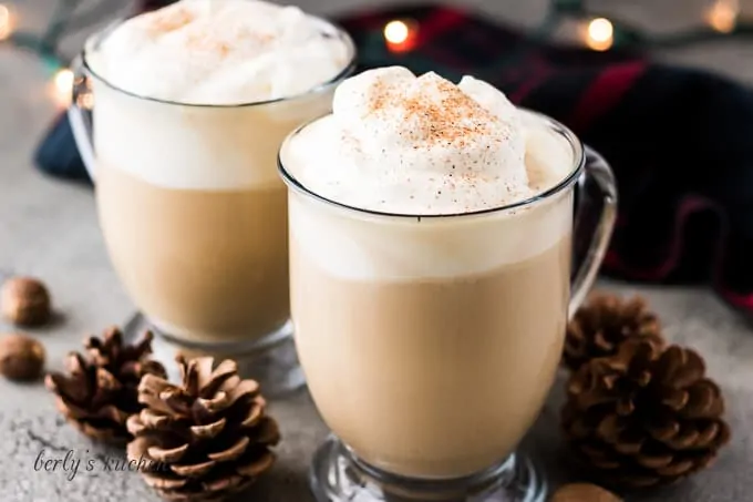 Two eggnog lattes served in clear mugs with whipped cream.