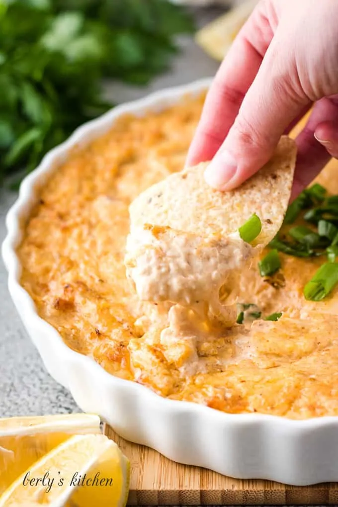 A tortilla chip being dipped into the hot crab dip.