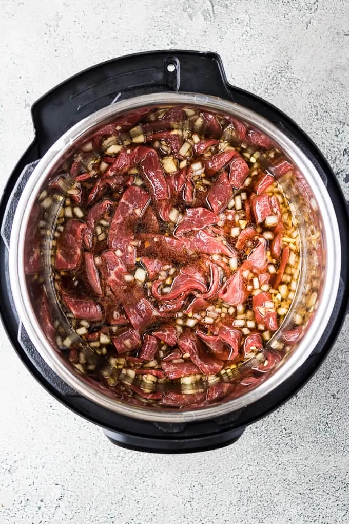 Uncooked beef and sauce in the pressure cooker liner.