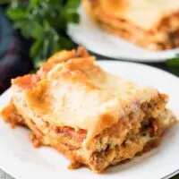 Slices of lasagna on small plates surrounded by fresh parsley.