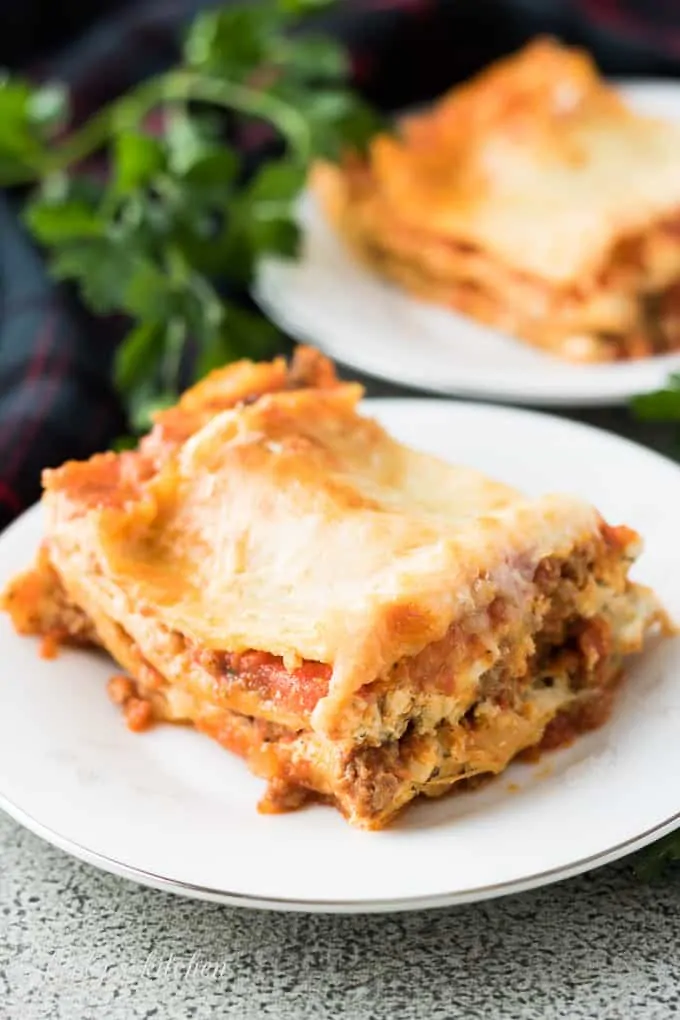 Slices of lasagna on small plates surrounded by fresh parsley.