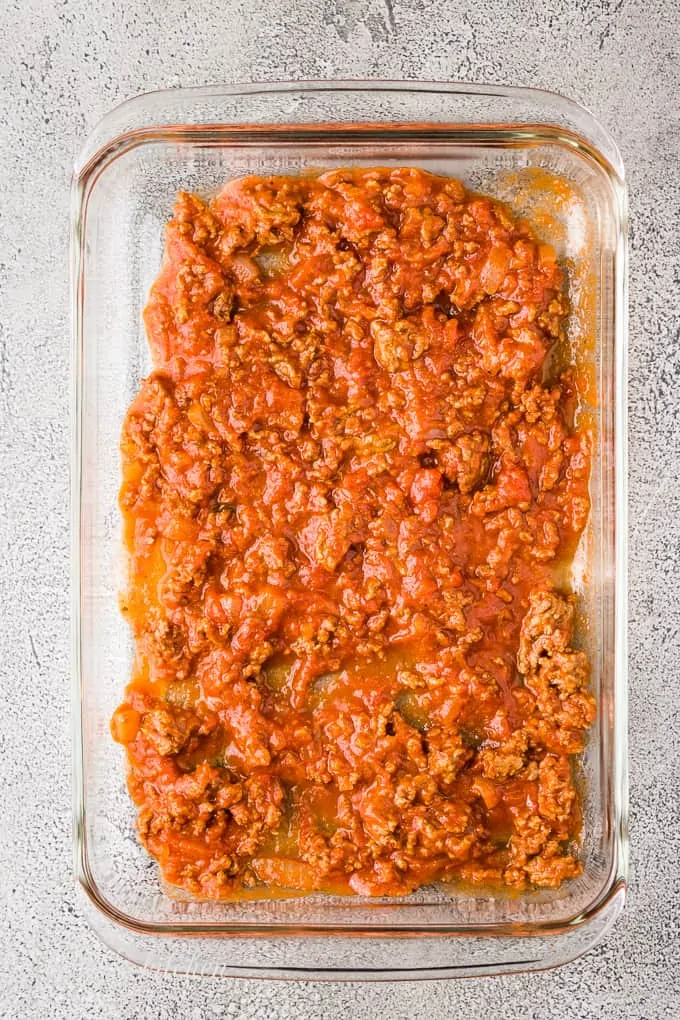 A scoop of even spread marinara in a baking dish.