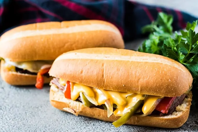 Two philly cheesesteak sandwiches with provolone or cheddar cheese sauce.