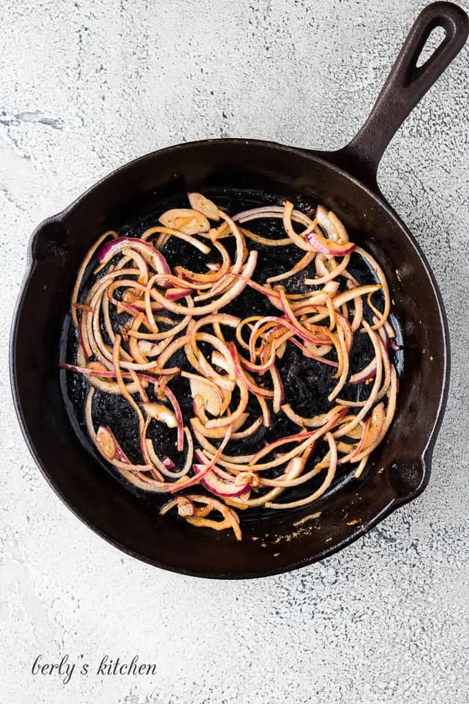 Sliced red onions are sauteing in the cast iron skillet.