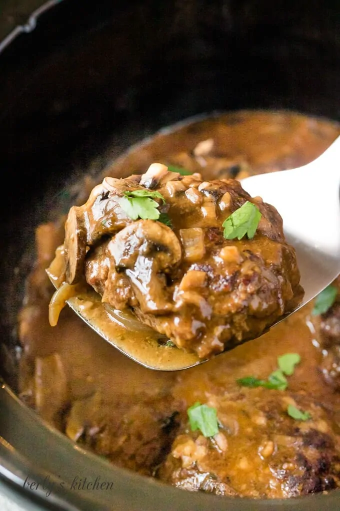 One cooked salisbury steak being lifted from the slow cooker.