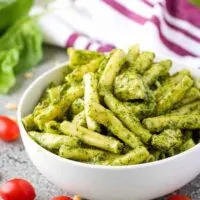 The pesto pasta in a bowl surrounded by cherry tomatoes.