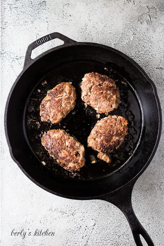 The beef mixture formed into patties cooking in the skillet.