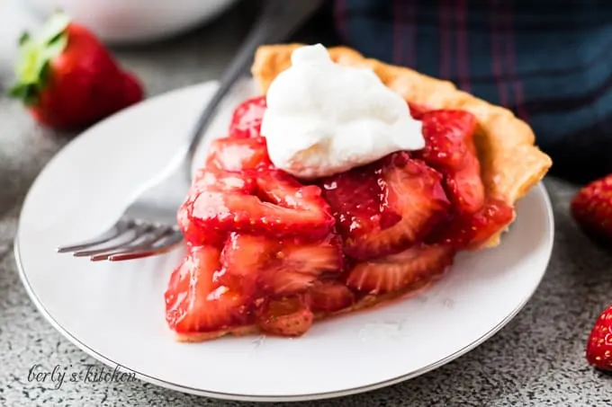 The strawberry pie topped with whipped cream on a plate.