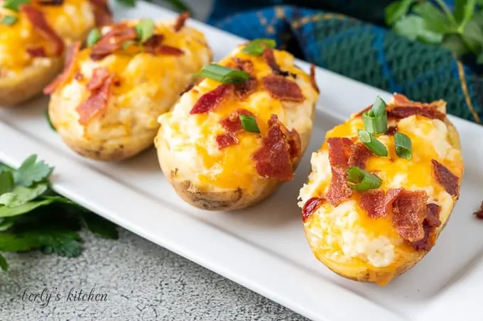 Four twice baked potatoes with cheese on a rectangular platter.