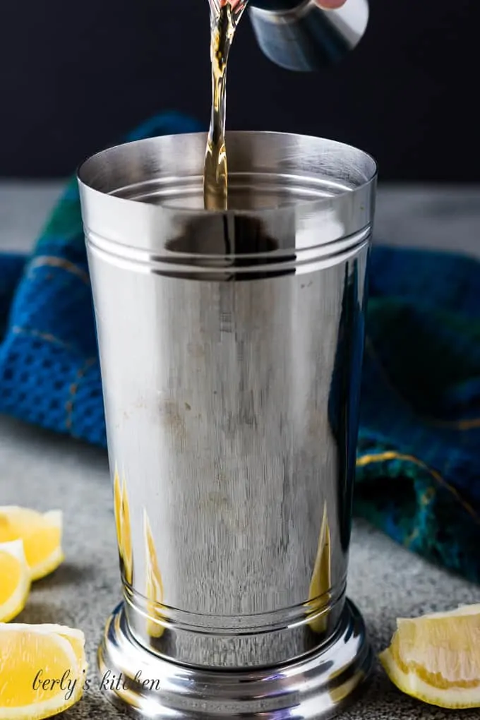 The whiskey being poured into a chrome shaker with ice.