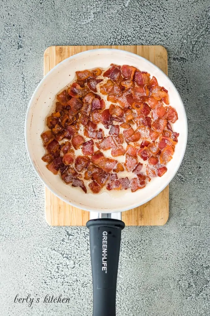 Chopped bacon pieces being cooked in a small white saucepan.