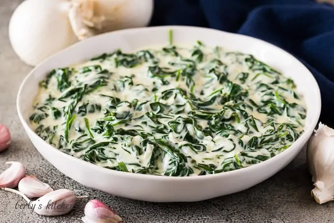 The creamed spinach in a bowl surrounded by garlic cloves.