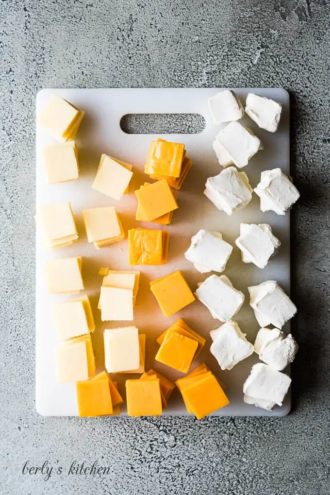 The cheeses cut into small squares on a cutting board.