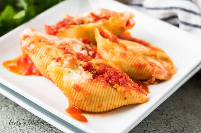 Four ricotta stuffed pasta shells on a decorative square plate.