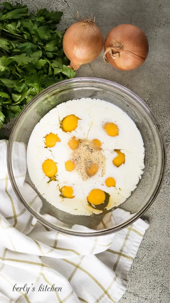 Twelve eggs and whole milk in a mixing bowl.