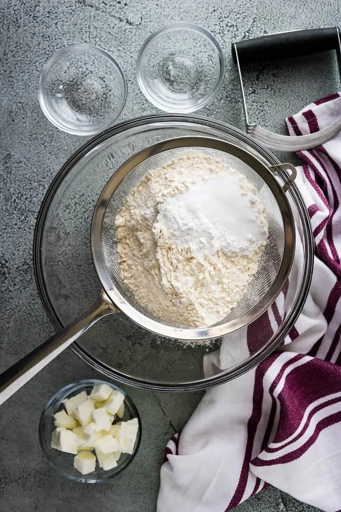 A wire mesh sieve with flour, baking powder, and salt over a bowl.