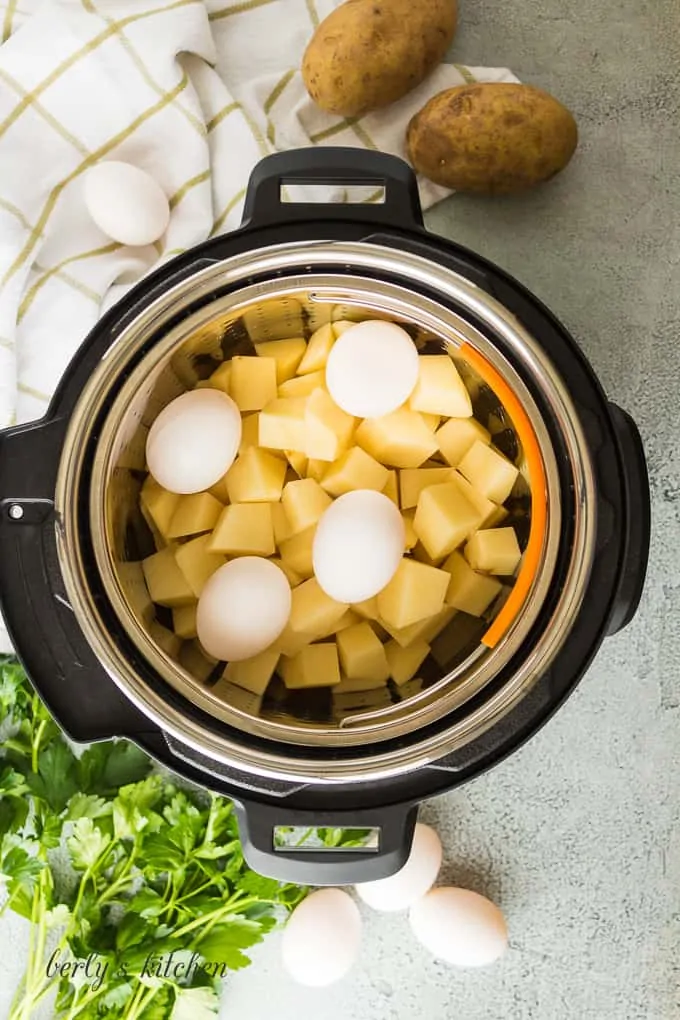 Ariel view of a pressure cooker with a basket of potatoes and 4 eggs on top.