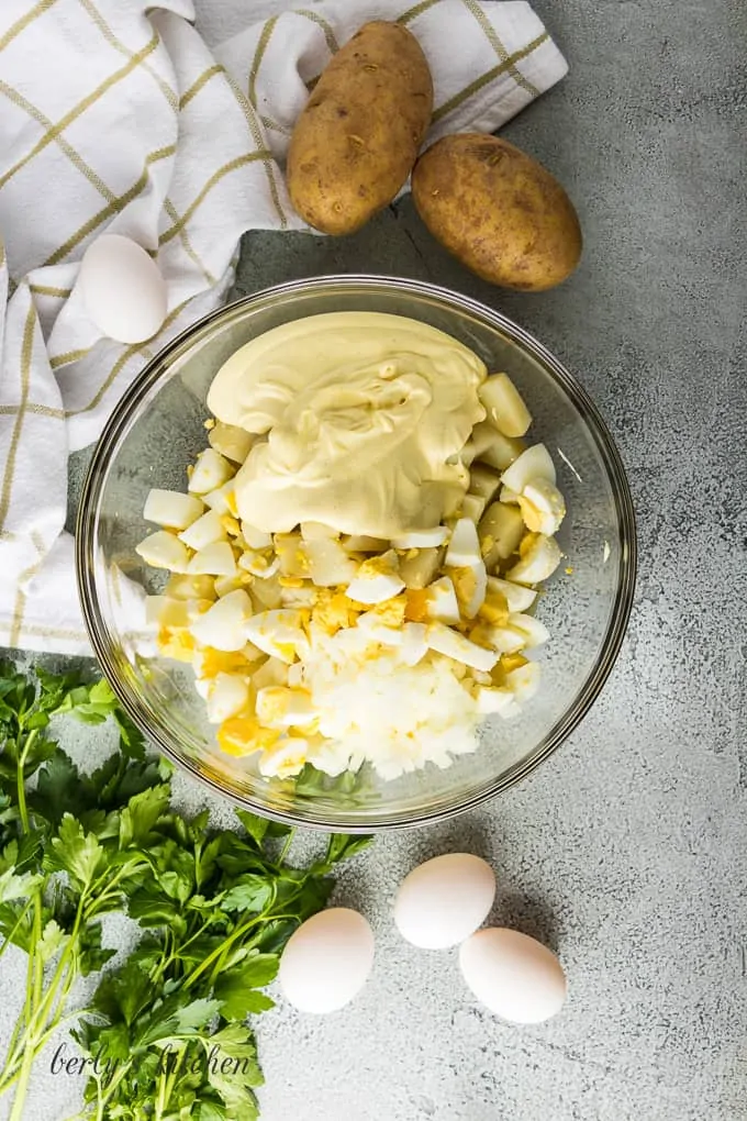 Ariel view of potatoes, eggs, onion, and dressing in a large bowl.