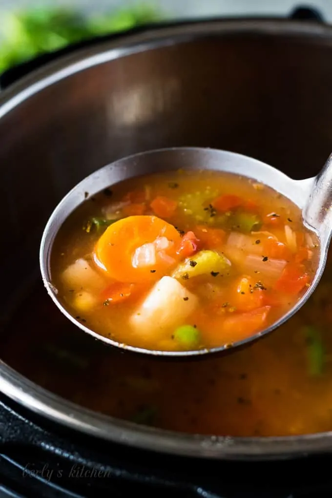 A scoop of the veggie soup in a metal ladle.