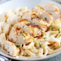 Plate of homemade fettuccine alfredo with sliced chicken on top.