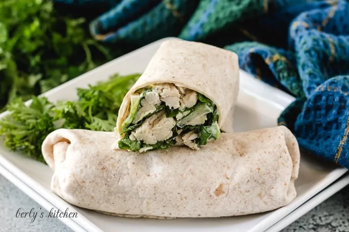 Two chicken caesar wraps on a square plate.