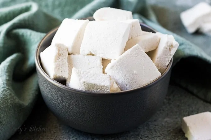 A green bowl filled with marshmallow squares.