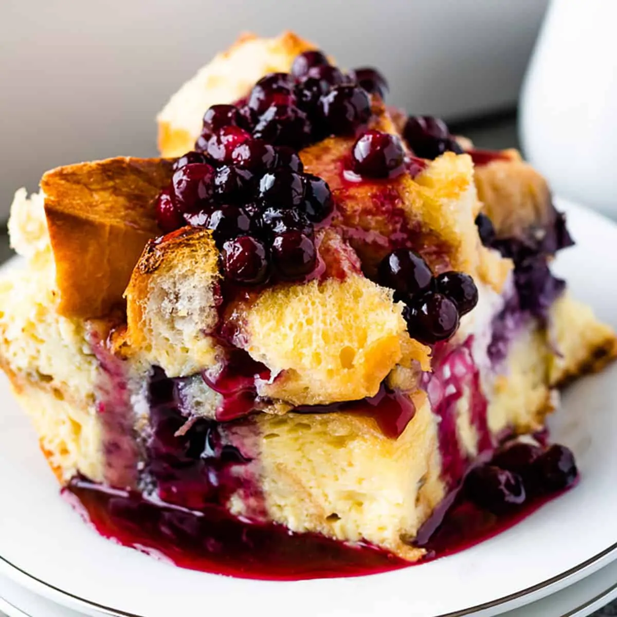 Large slice of french toast casserole topped with blueberry sauce on a white plate.