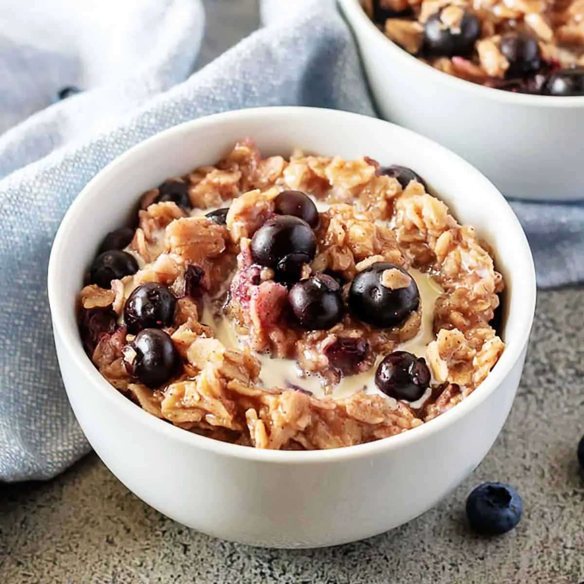 Two bowls of blueberry oatmeal topped with fresh blueberries.