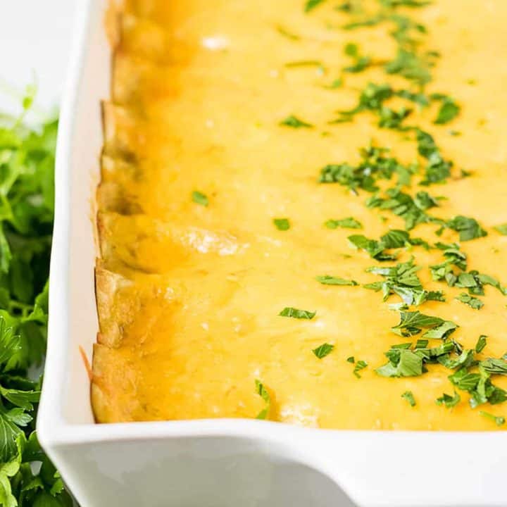 Baking pan full of cheesy breakfast enchiladas topped with chopped parsely.